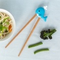 Training chopsticks with a whale topper beside a bowl of noodles and vegetables.