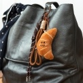 Plush croissant bag charm with brown cord strap and metal clip attachment