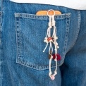 Beige cord phone strap with bead and flower charms shown hanging from a phone in a denim pocket.
