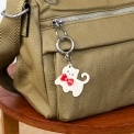 Cream cat-shaped keyring with red bow and silver ring attachment.