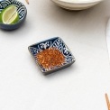 Square ceramic dipping bowl with a blue leaf pattern shown with chilli flakes.