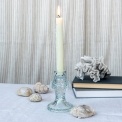 Pale blue fish-shaped glass candlestick holding a lit white candle on a tabletop