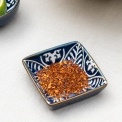 Square ceramic dipping bowl with a blue leaf pattern shown with chilli flakes.