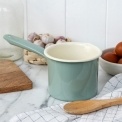 Alt text: Pistachio green enamel milk pot with long handle on a kitchen worktop.