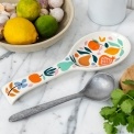 White ceramic spoon rest with a colourful fruit and leaf design.