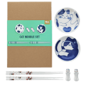 Two cat-themed dipping bowls, two pairs of chopsticks, and two cat-shaped rests beside a brown box.