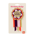Colourful birthday badge with a gold centre reading ‘It’s My Birthday!’ and ribbons displayed with its packaging.