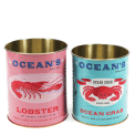 Two Ocean’s Brand storage tins featuring lobster and crab illustrations in pink and blue.