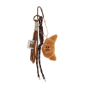 Plush croissant bag charm with brown cord strap and metal clip attachment
