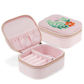 Open pink jewellery box with embroidered floral design, ring rolls and storage compartments.