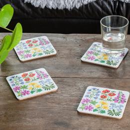 Four white wood and cork coasters featuring floral pattern on table with drink