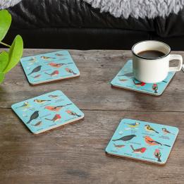 Four light blue wood and cork coasters featuring garden bird pattern on table with drink