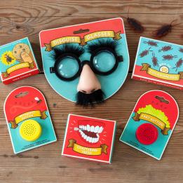 A selection of novelty toys including joke glasses with a nose and moustache, fake teeth, and other small trinkets, laid out on a wooden surface.