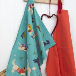 Cotton tea towel with colourful illustrations of dogs in winter clothing, hanging on hook