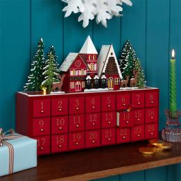 Red advent calendar with 24 gold-numbered drawers and a snowy village scene on top