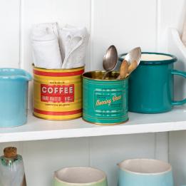 Two vintage coffee tins repurposed as utensil holders on a kitchen shelf.