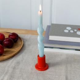 red ceramic candle holder with a cylindrical shape and wide flat base, holding a lit candle