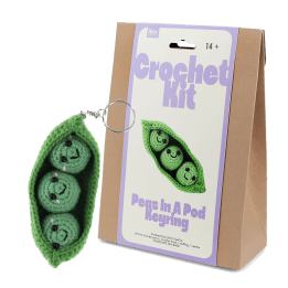 Crochet kit packaging placed beside finished green peas in a pod keychain 