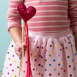 Kid holding a red heart wand with glittery top and ribbon streamers 