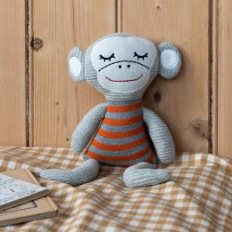 Knitted monkey toy with a grey body and wearing an orange and grey striped shirt.