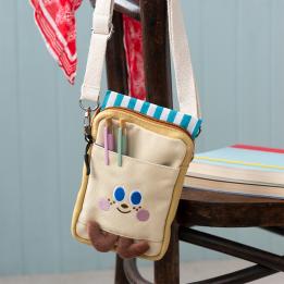 Beige and yellow crossbody bag with a front pocket featuring a smiling face design and two small brown plush feet at the bottom.