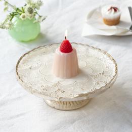 Pink jelly-shaped candle topped with a decorative red strawberry displayed on a decorative cake stand.