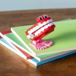 Wind-up toy shaped like red chattering teeth with white teeth, googly eyes, and pink feet