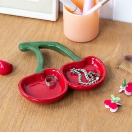 Red ceramic trinket dish shaped like two cherries with green stems displayed with ring and bracelet. 