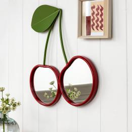Wall mirror shaped like two cherries with red frames and green leaf detail hanging on the wall.