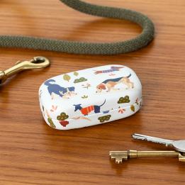 Mini travel case with playful dog illustrations on a wooden surface beside keys.