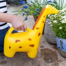 A yellow giraffe‑shaped watering can placed on a patio near plants.