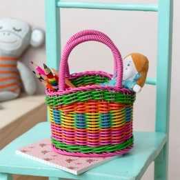 A small woven plastic basket with a pink handle and multicoloured striped body