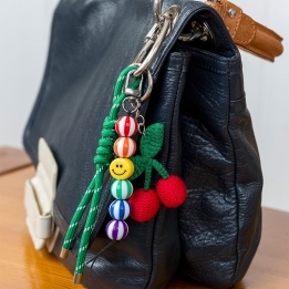 Crochet cherry bag charm with green cord strap, colourful beads attached to the bag 