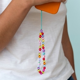 Colourful beaded phone strap attached to an orange phone, featuring heart beads and letter beads spelling “HAPPY”