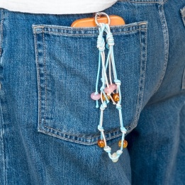 Blue and tan cord phone strap with decorative beads shown hanging from a phone in a denim pocket.