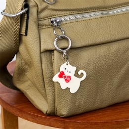 Cream cat-shaped keyring with red bow and silver ring attachment.