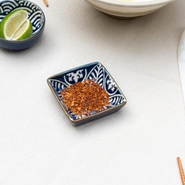 Square ceramic dipping bowl with a blue leaf pattern shown with chilli flakes.
