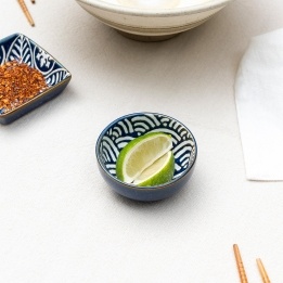 Round ceramic dipping bowl with blue wave pattern shown with lime wedges.