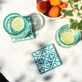 Turquoise ceramic tile coasters with white pattern beside two glasses of lemon water.