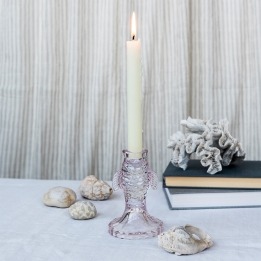 Pale pink fish-shaped glass candlestick holding a lit white candle on a tabletop