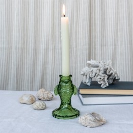 Green fish-shaped glass candlestick holding a lit white candle on a tabletop