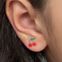 Stick-on earrings in cherry and lightning bolt shapes on a kid’s ear