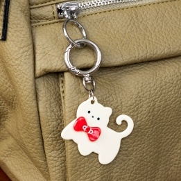 Cream cat-shaped keyring with red bow and silver ring attachment.