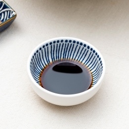 Round ceramic dipping bowl with blue line pattern shown with soy sauce.