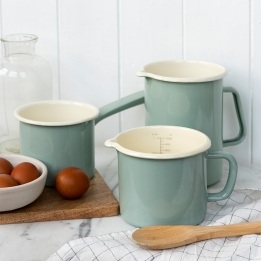 Alt text: Set of pistachio green enamel measuring jugs and milk pot on a kitchen worktop.