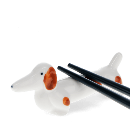 Chopsticks resting on a ceramic sausage dog–shaped chopstick rest.