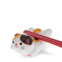 Chopsticks resting on a ceramic cat–shaped chopstick rest.