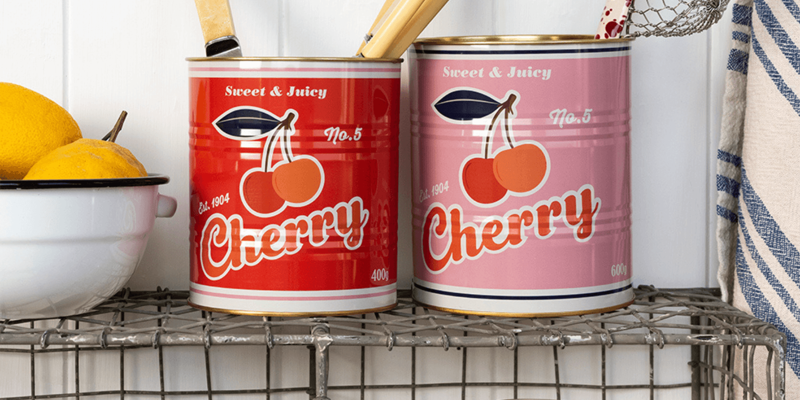 Two storage tins with a bold cherry print, filled with kitchen utensils