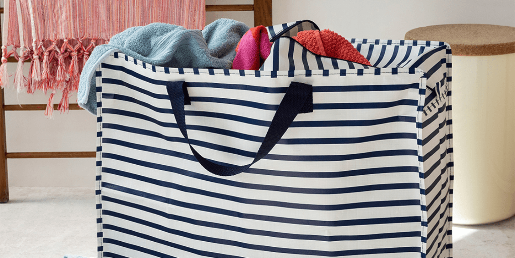 A blue and white striped storage bag with blankets poking out of the top