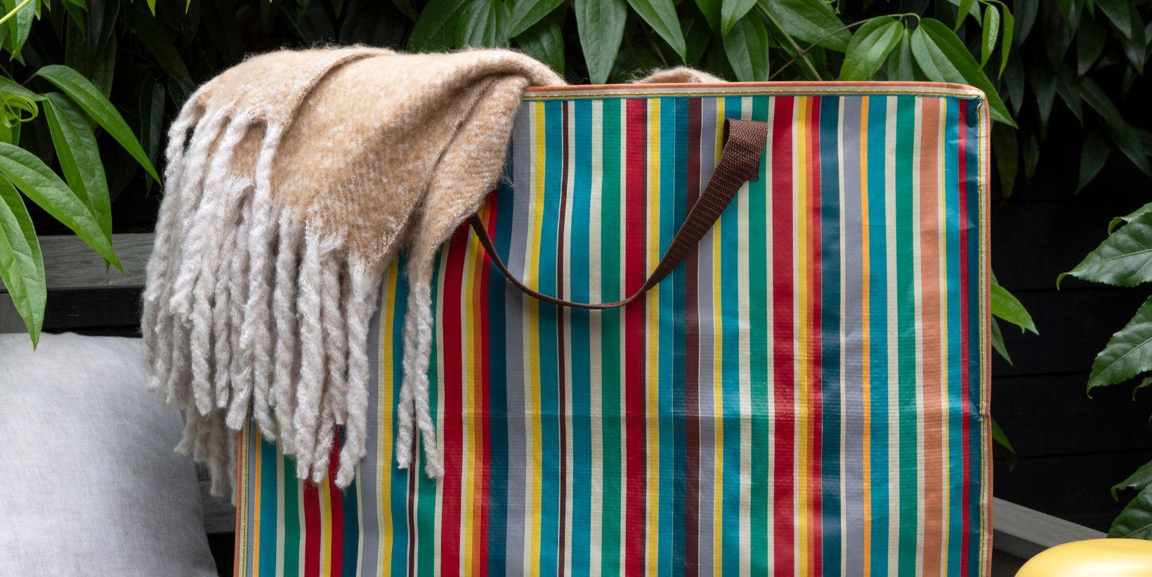 A large storage bag with multicoloured stripes with a blanket poking out of the top